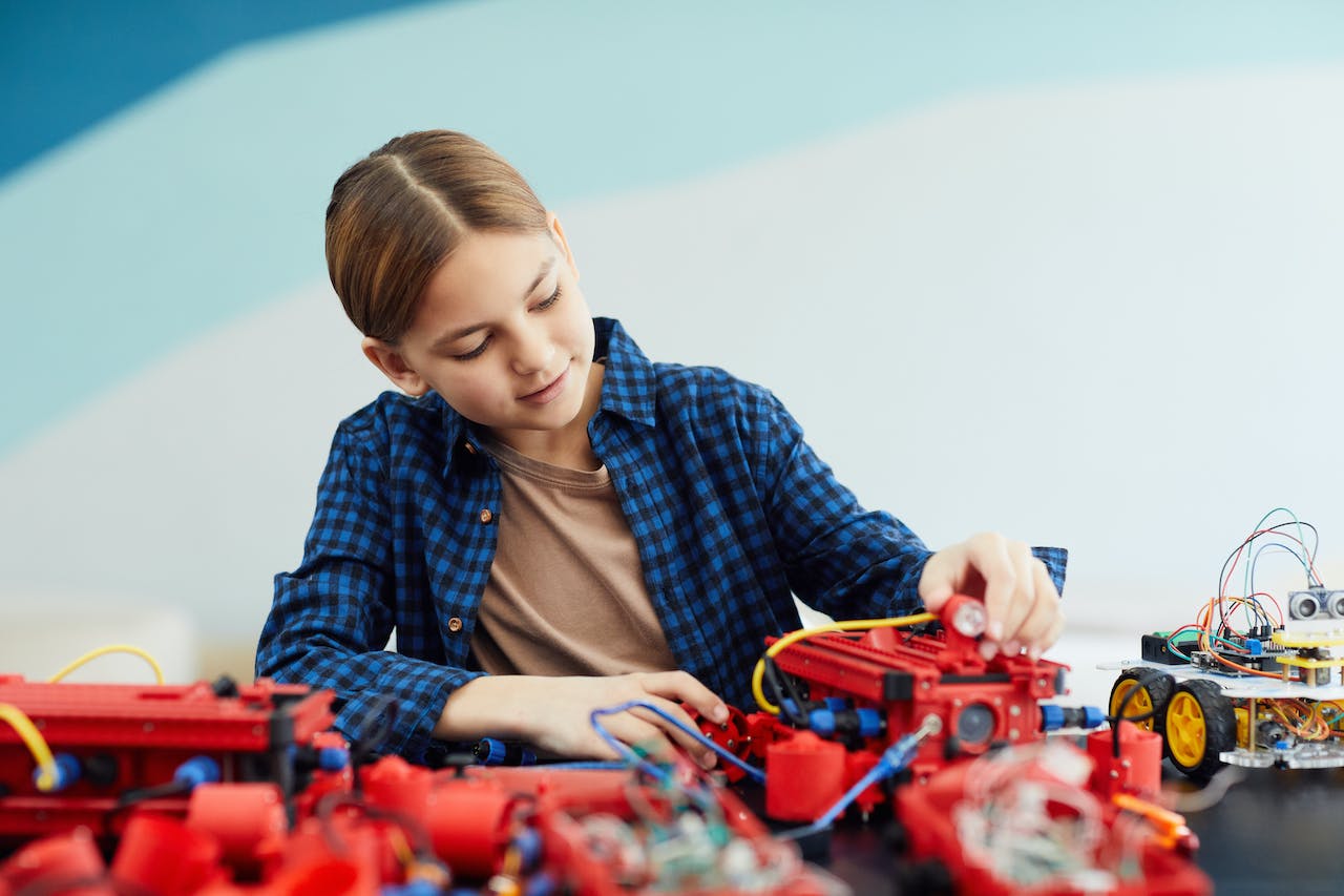 A Girl Looking at a Wheeled Toy with Wires